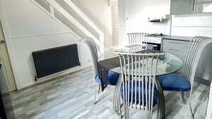 Eine moderne Küche mit Gasherd, Backofen und Mikrowelle. Es gibt einen Essbereich mit einem Glastisch und Metallstühlen. Eine Treppe mit weißen Geländern führt zu einer oberen Ebene.
