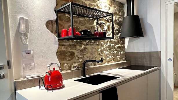 A modern kitchen with a stone wall backsplash, a black hanging light, and a red kettle on the counter.