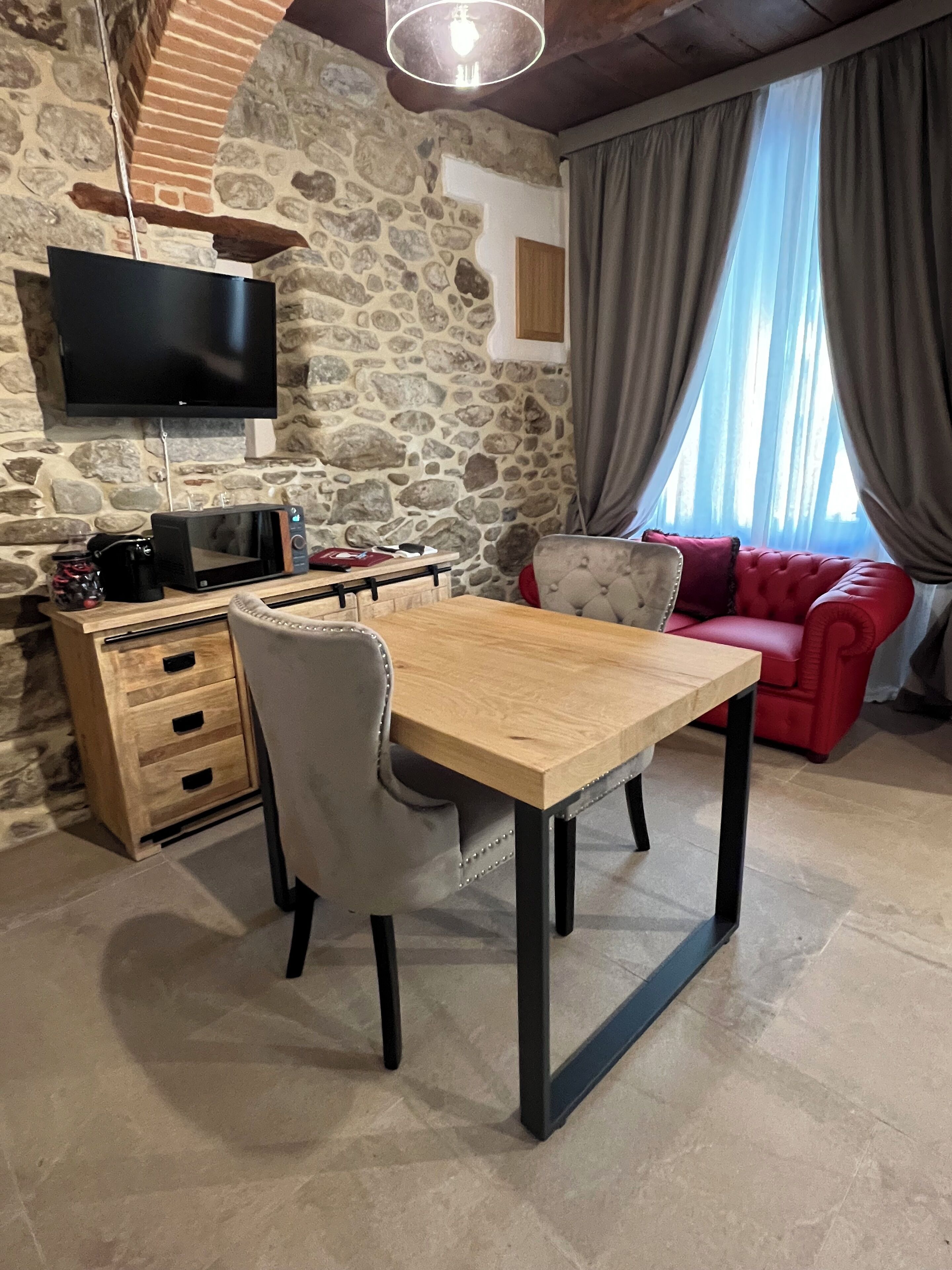 Una sala de estar acogedora con una pared de piedra, una mesa de madera, un sofá rojo y un televisor montado.