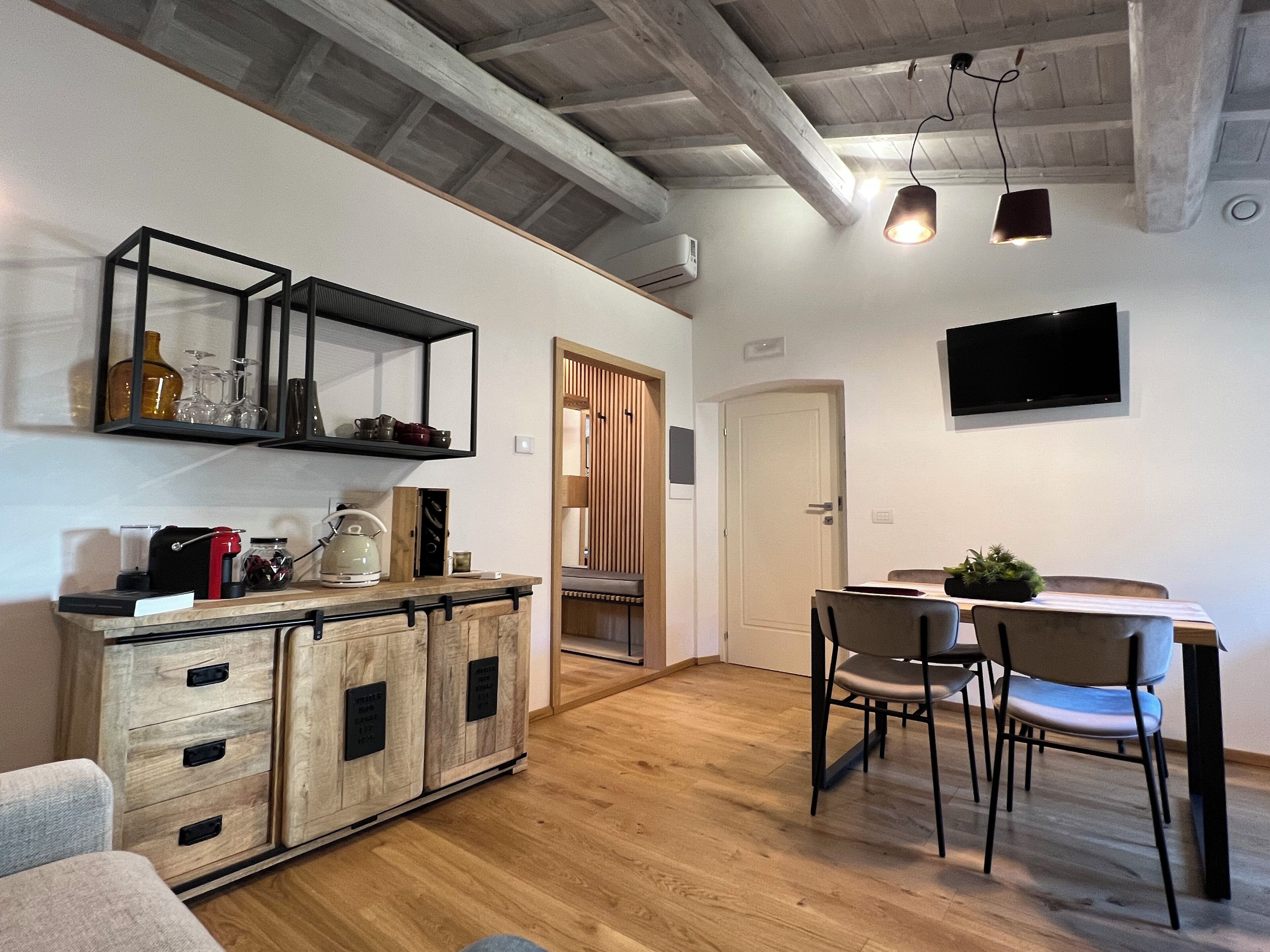 Une cuisine moderne avec des meubles en bois, un coin repas comprenant une table et des chaises, et un téléviseur fixé au mur.