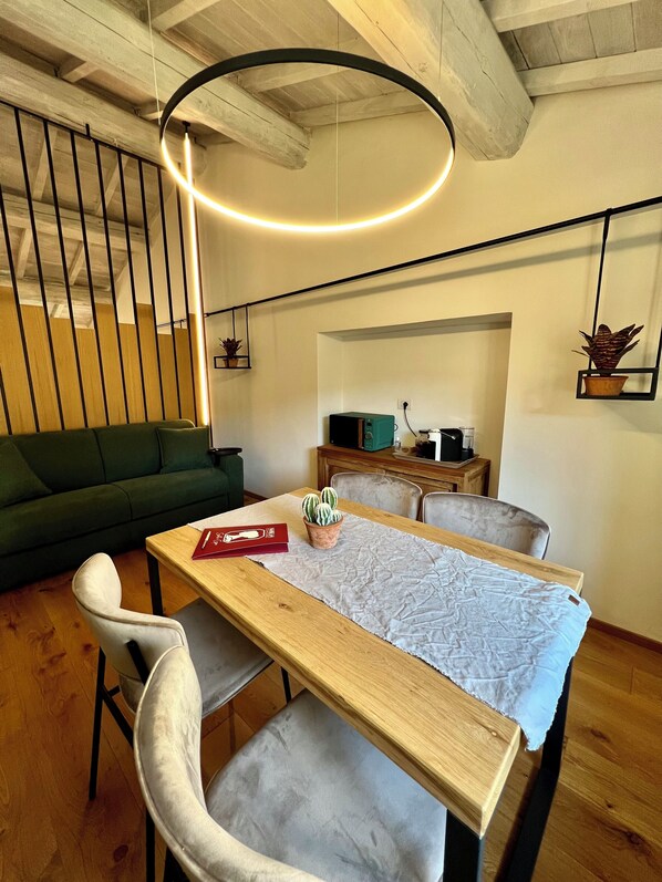 A modern living space with a wooden dining table, a green sofa, and a kitchen area in the background.