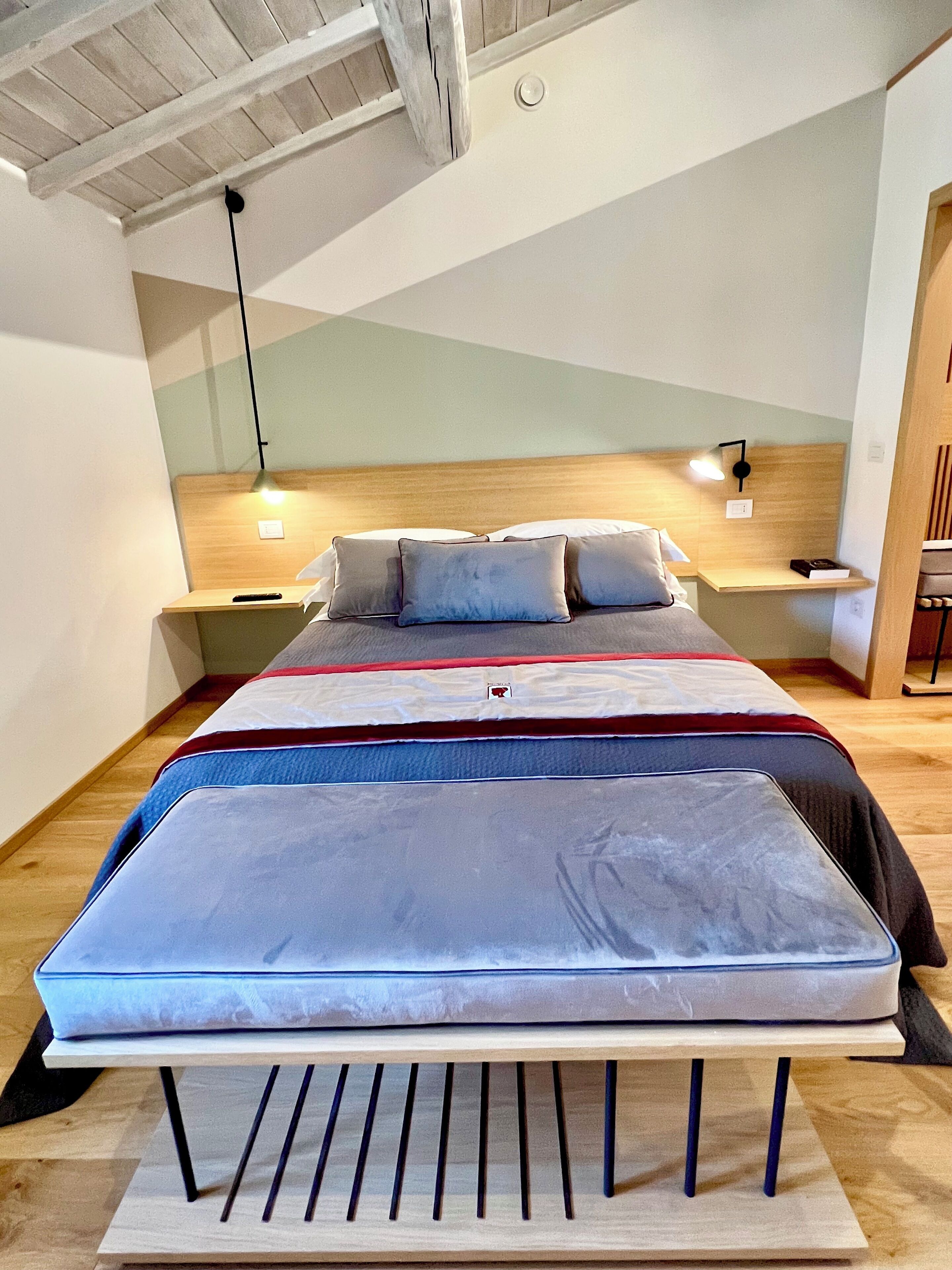 A modern bedroom with a large bed, wooden headboard, bedside tables, and a hanging light fixture.