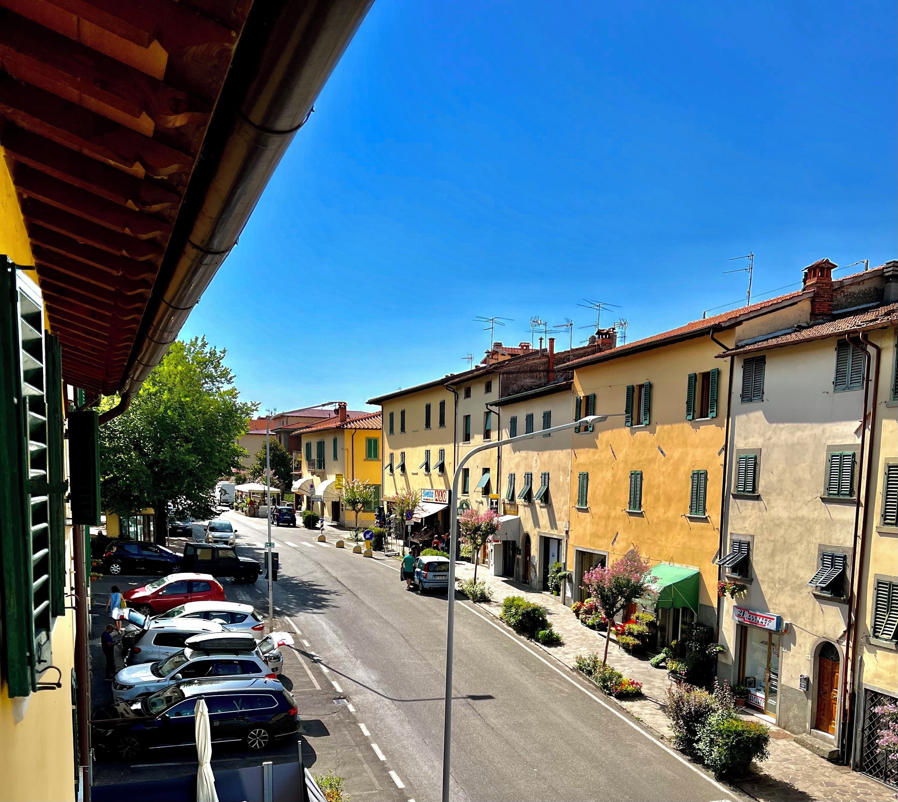 Une vue de rue avec des voitures garées, des bâtiments avec des volets et un ciel bleu dégagé.
