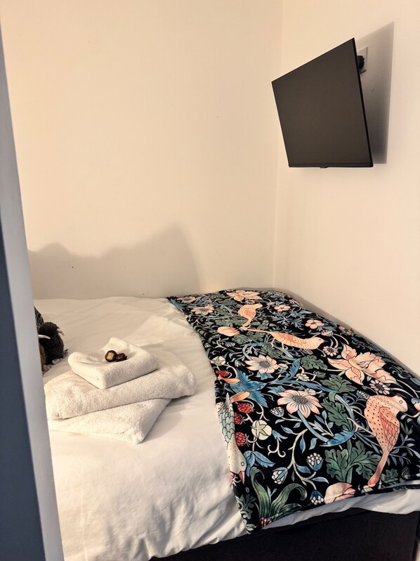 Una cama pequeña y ordenada con un edredón estampado con motivos florales y una toalla blanca.