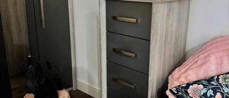 Un dormitorio con cama, cómoda, taburete pequeño y mesita de noche con velas.
