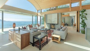 Un salon moderne doté d’une grande fenêtre donnant sur la mer, d’une cheminée et d’un plafond en bois.