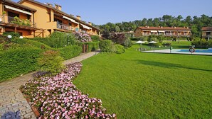 Un hotel con un césped cuidado, piscina y un jardín con flores rosadas.
