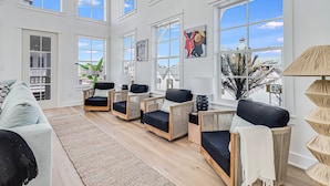 A spacious living room with large windows, a light-colored sofa, and several wicker chairs.