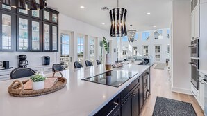 A modern kitchen with a large island, dark cabinetry, and a view to the living area.