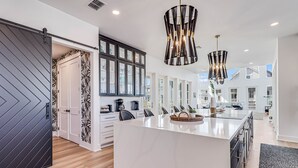 A modern kitchen with a large island, dark cabinets, and pendant lighting.