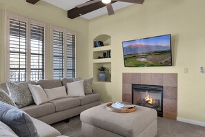 A living room with a fireplace, a sofa, a television, and a bookshelf. - 3BR Legacy Villas condo with pool, patio, Wi-Fi, and mountain charm (La Quinta)