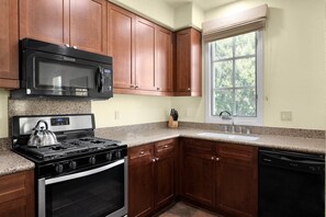 A kitchen with wooden cabinets, a stainless steel microwave, a gas stove, and a dishwasher. - 3BR Legacy Villas condo with pool, patio, Wi-Fi, and mountain charm (La Quinta)