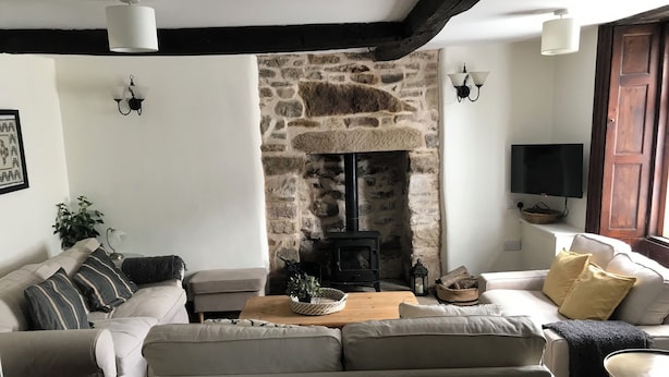 A cozy living room with a stone fireplace, a sofa set, a wooden coffee table, and a television mounted on the wall. - Hunters Cottage (Bakewell)