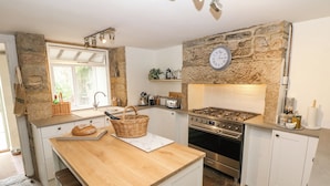 A kitchen with a stone wall, a wooden island, a gas stove, and white cabinets. - Hunters Cottage (Bakewell)