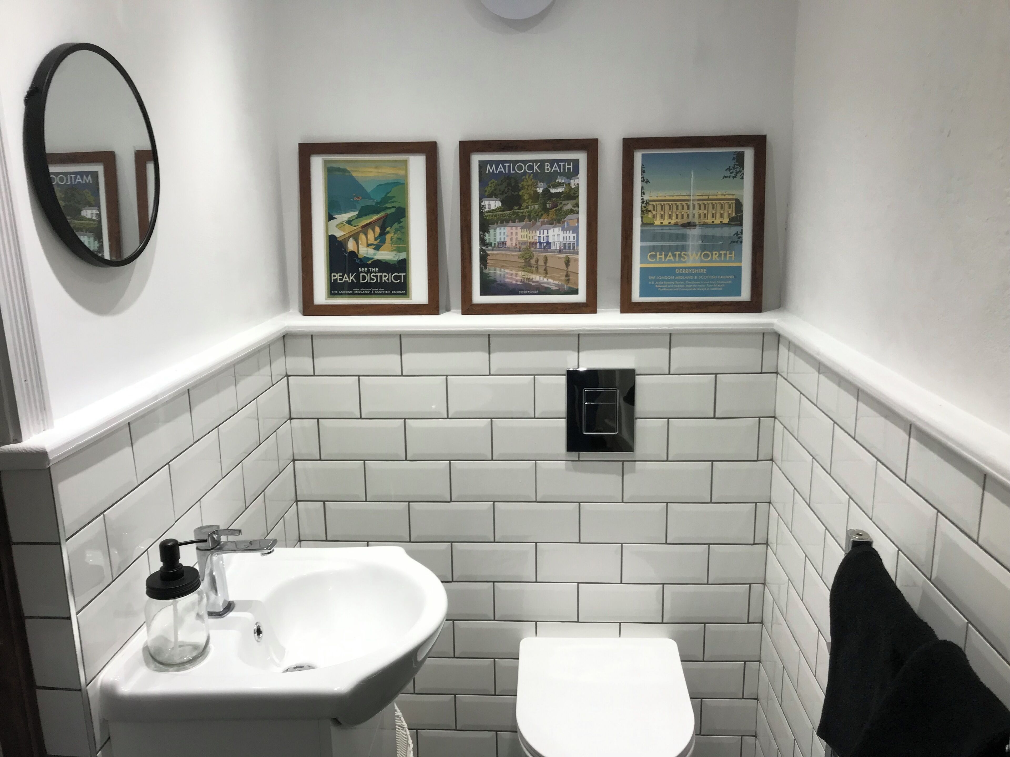 Een badkamer met een witte wastafel, een toilet en drie ingelijste posters aan de muur.