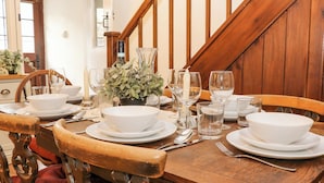A dining table set with white bowls, plates, and cutlery, surrounded by wooden chairs and a potted plant. - Hunters Cottage (Bakewell)