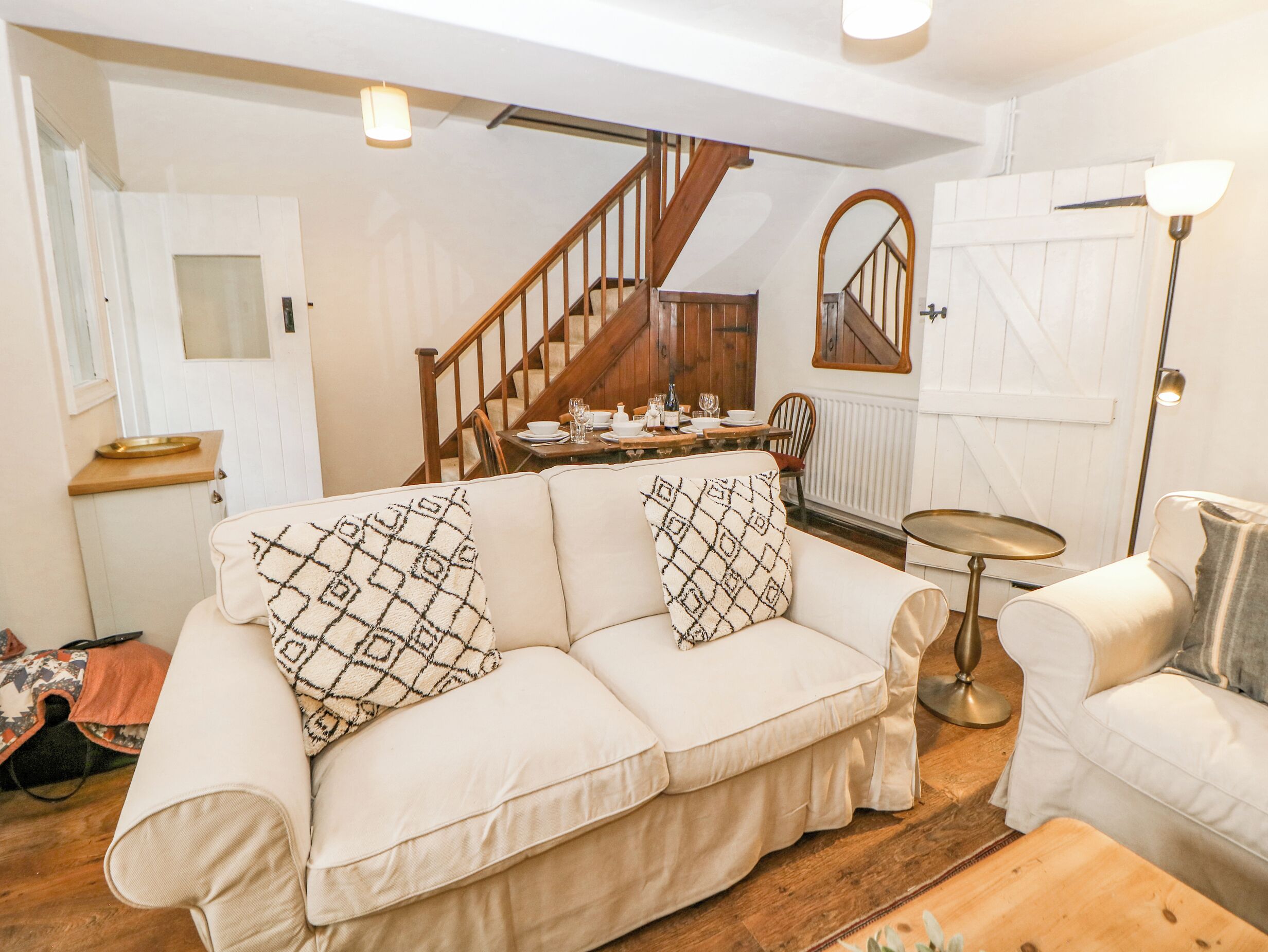 A cozy living room with a sofa, a dining table set for four, a staircase, and a small round table.