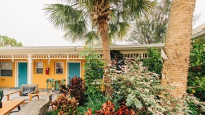 A courtyard with a yellow building, outdoor seating, and a palm tree. - Little Havana Retreat, Steps from the Beach - King Size Bed & Gulf Bliss! (Indian Rocks Beach)