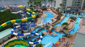 A water park with multiple pools and slides, surrounded by palm trees and a building with balconies. - Little Havana Retreat, Steps from the Beach - King Size Bed & Gulf Bliss! (Indian Rocks Beach)
