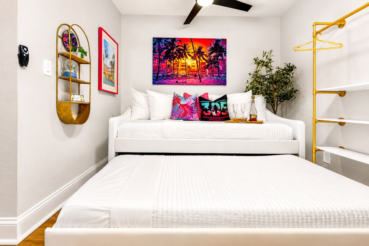 Une chambre avec un lit blanc, un tableau coloré, une étagère dorée et une plante.