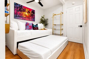 Ein Schlafzimmer mit einem weißen Bett, einem farbenfrohen Gemälde, einer Pflanze und einer goldenen Regalwand.