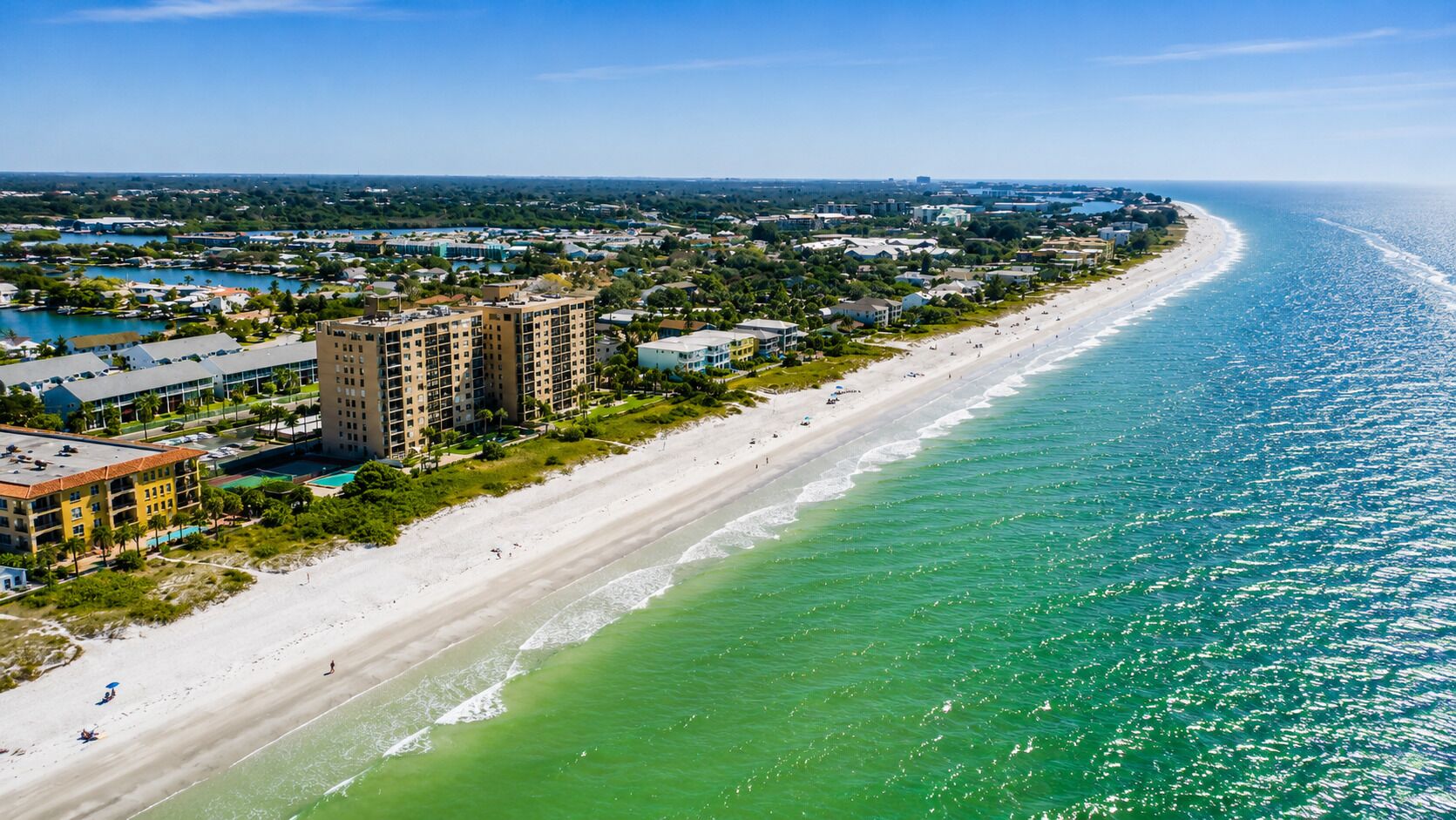 A coastal resort with beachfront properties, a sandy beach, and a clear view of the ocean.