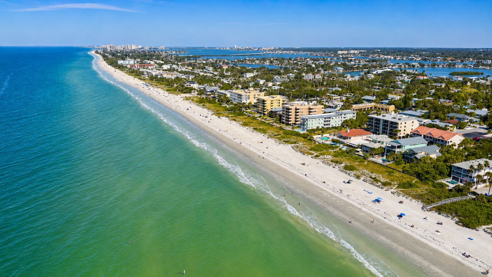 An aerial view of a coastal area with a beach, buildings, and a marina.