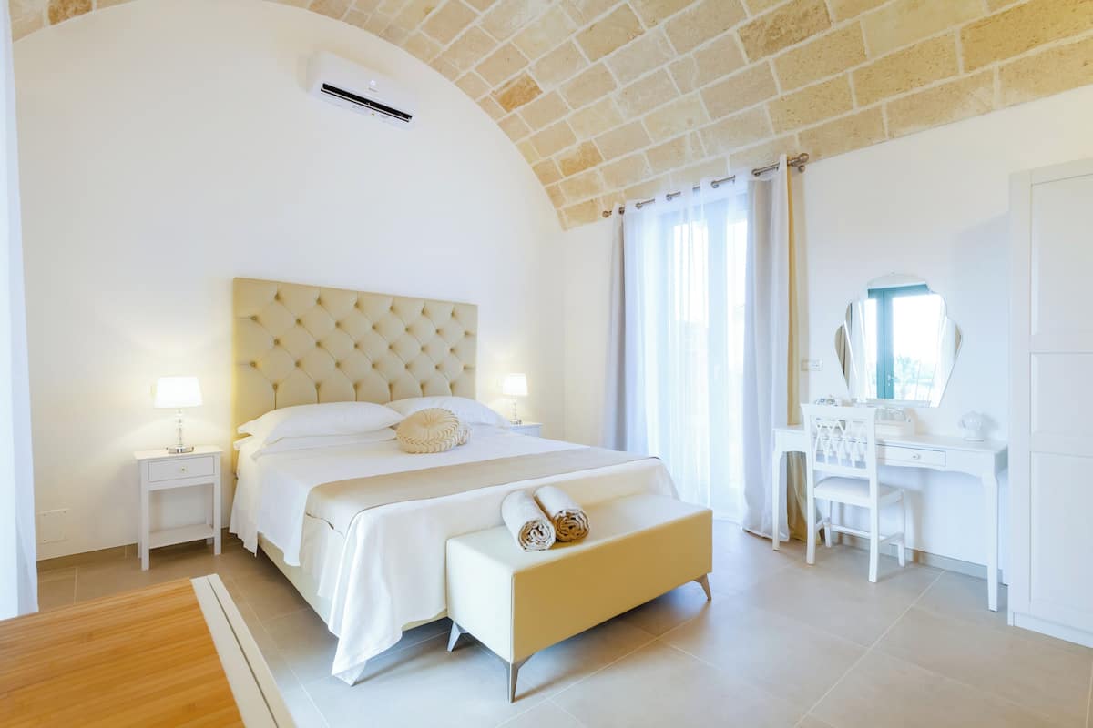 A modern bedroom with a large bed, bedside tables, a desk, and a chair.