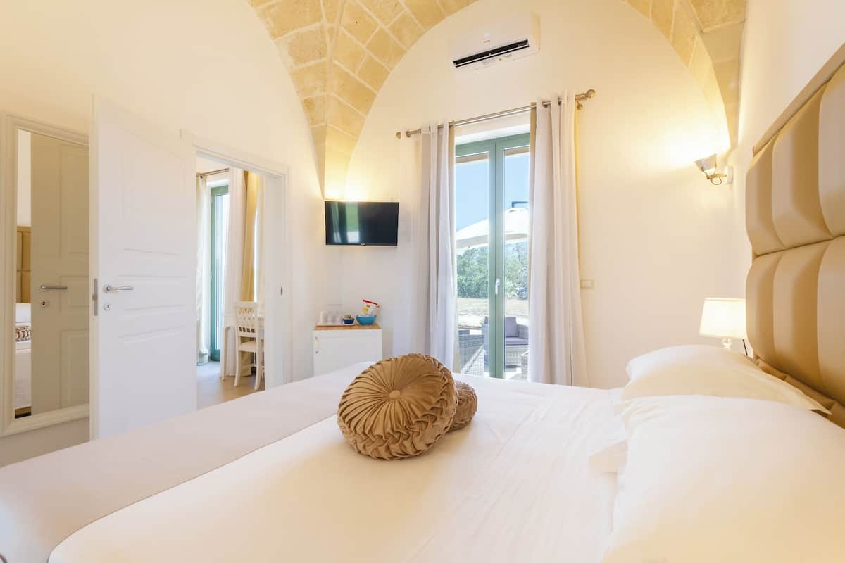 A hotel room with a large bed, a flat-screen TV mounted on the wall, and a balcony with a view.