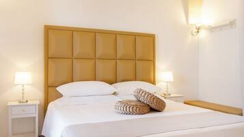 Una cama bien hecha con cabecera capitonada, dos mesitas de noche con lámparas y un banco al pie de la cama.