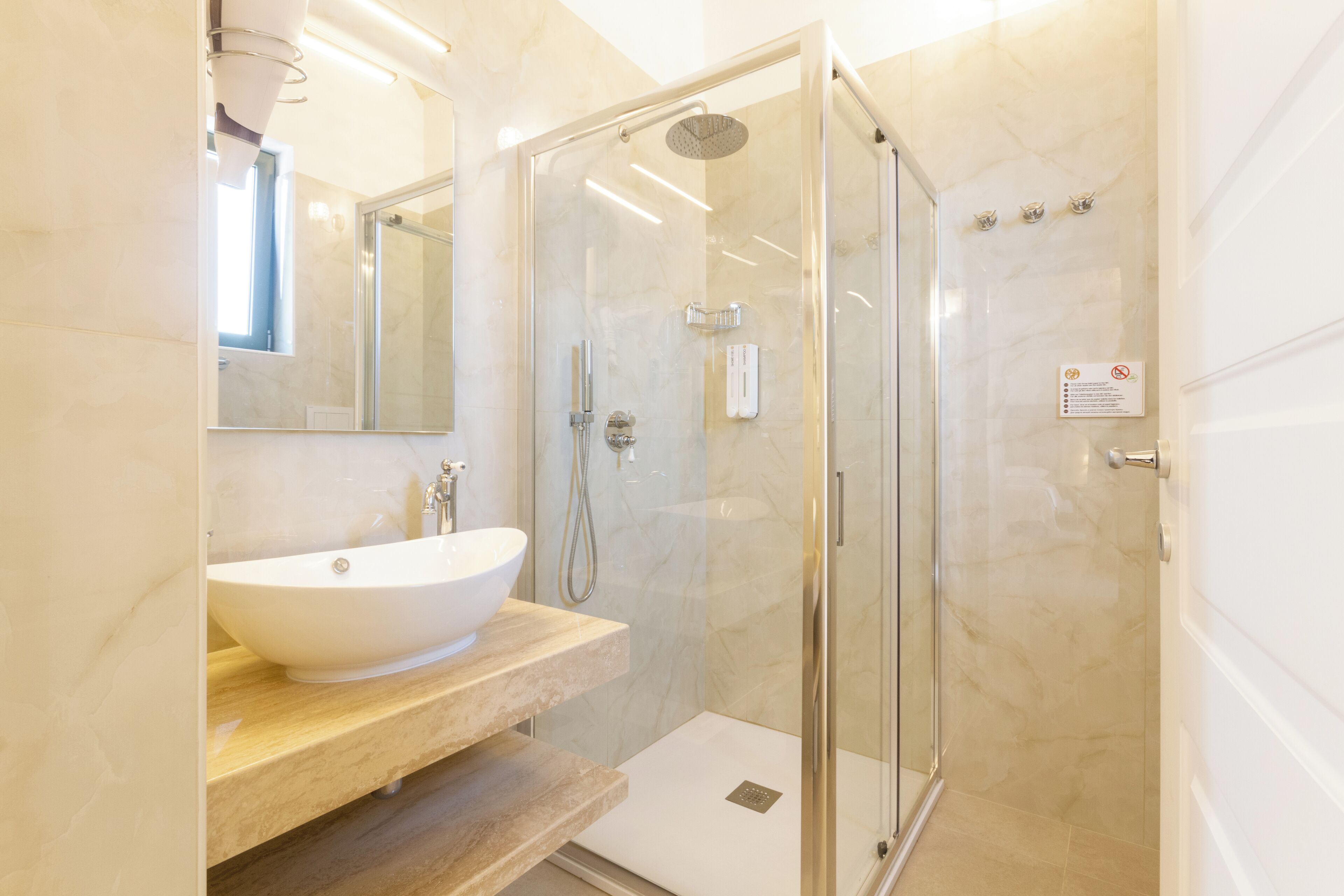 A modern bathroom with a glass-enclosed shower, a white sink, and a marble-tiled wall.