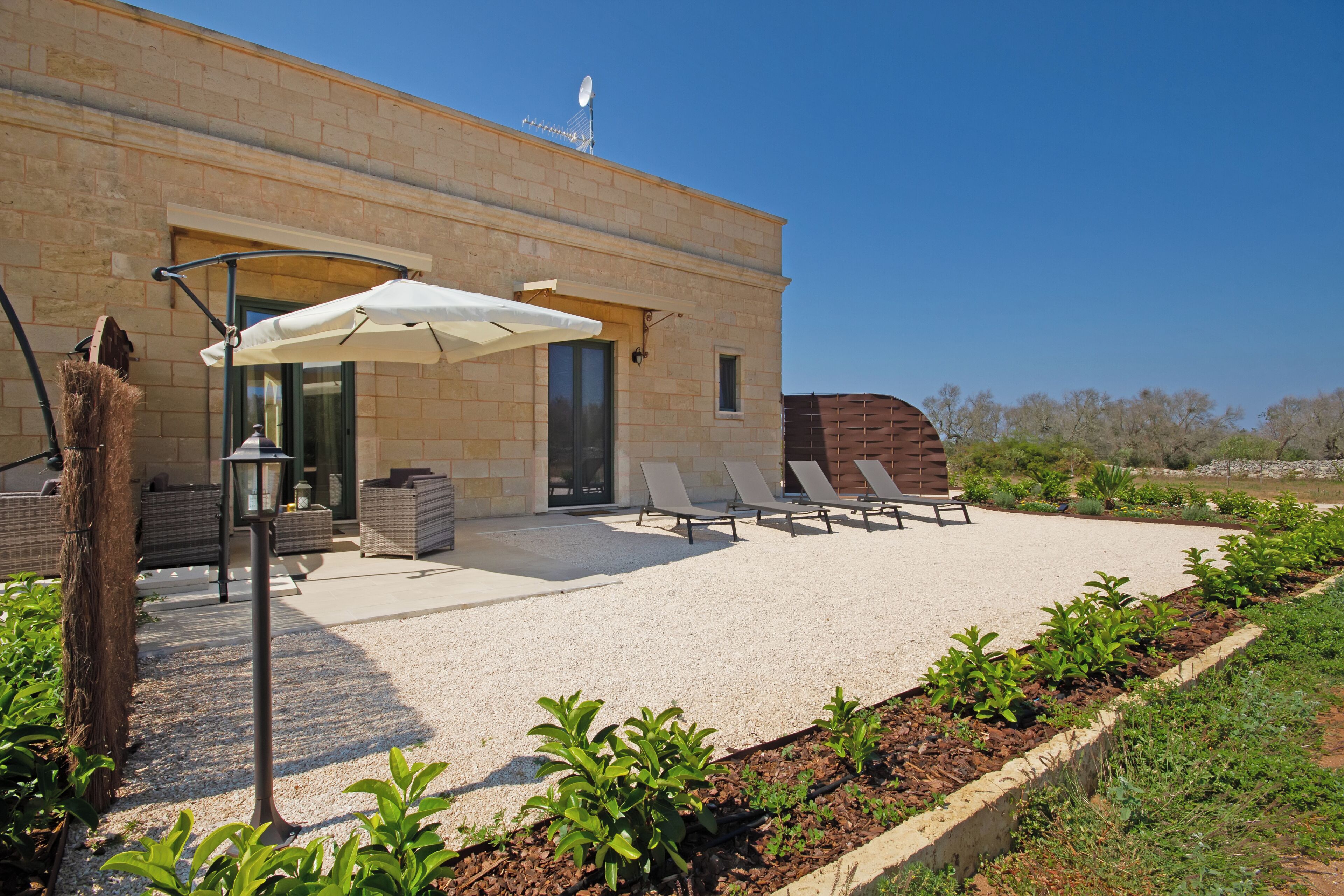 Een modern gebouw met een patio voorzien van loungestoelen, een barbecue en een pergola met parasols.