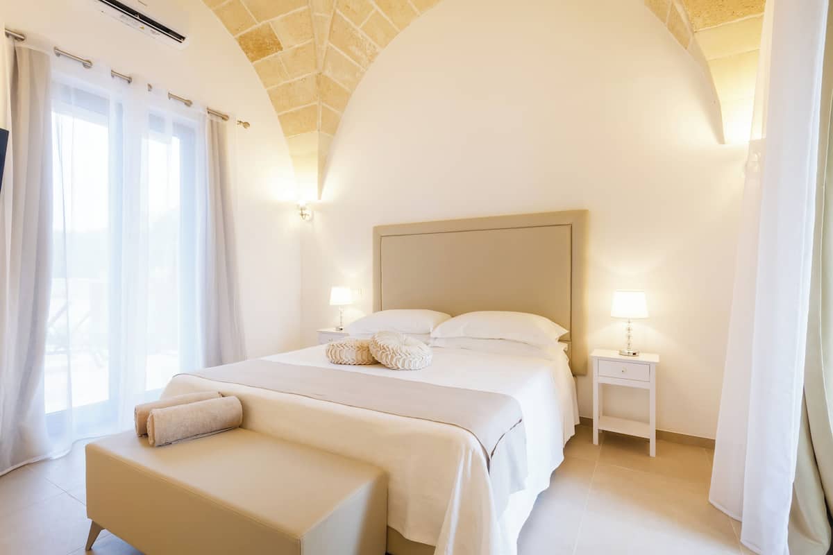 A hotel room with a large bed, a bedside table with a lamp, and a window with curtains.