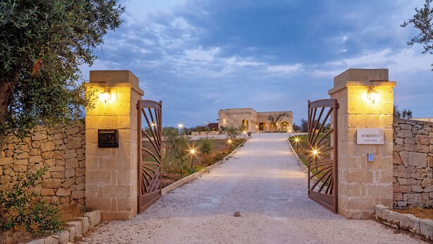 A gravel pathway leading to a building with stone walls and two illuminated gates. - Tenuta Dorolivo Guest House e B&B (Giurdignano)
