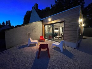 A modern house with a gravel patio, two white plastic chairs, and a red plastic chair. - Gîte Le Ballandeau (Ballan-Miré)