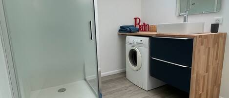 A modern bathroom with a glass shower enclosure, a built-in washing machine, and a wooden vanity.