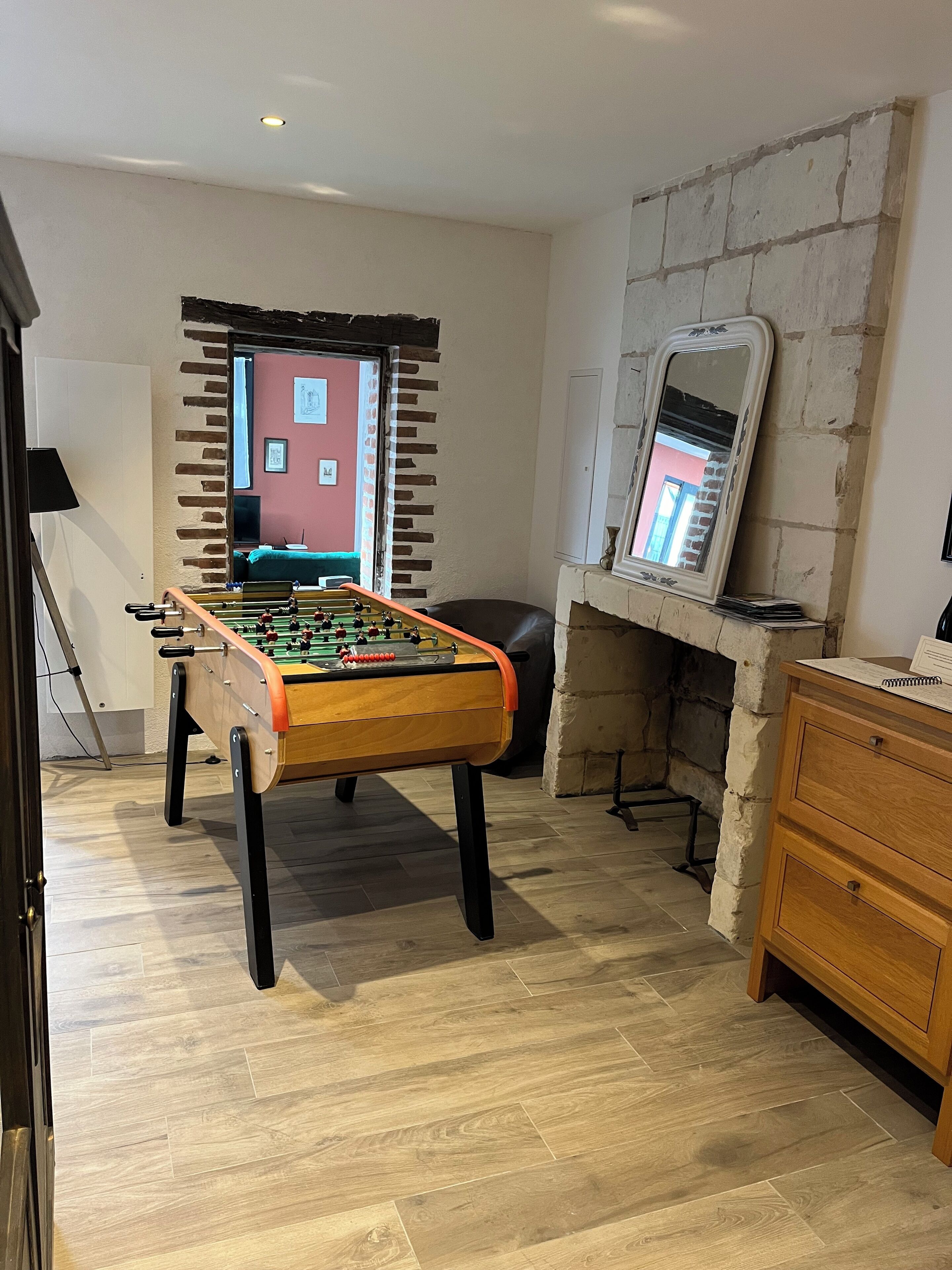 A room with a foosball table, a wooden cabinet, and a stone wall.