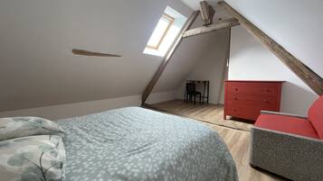Quarto com teto inclinado, cama com roupa de cama estampada, cômoda vermelha e uma cadeira.