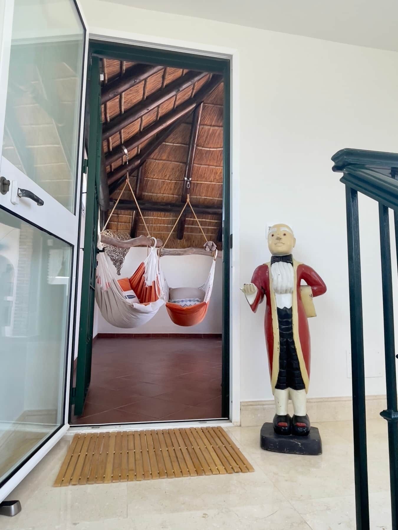 Una habitación con un amplio ventanal, un sillón colgante y una estatua de un hombre con un abrigo rojo.