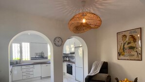 Eine geräumige Küche mit weißen Schränken, ein Essbereich mit einer Couch und einem Tisch, und ein großes Fenster, das für natürliches Licht sorgt.