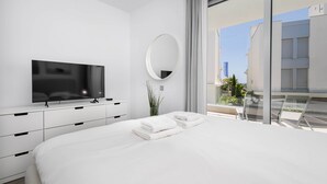 A modern bedroom with a large bed, a flat-screen TV, a mirror, and a balcony with a view of buildings. - RDR317 - Stylish 3 bedroom Le Mirage close to beach (Estepona)