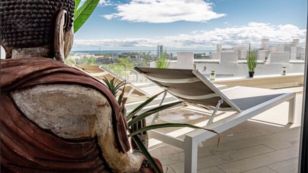 Une statue de Bouddha surplombe une terrasse sur le toit, où se trouvent des chaises longues et des plantes en pot.