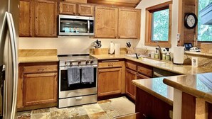 Una cocina con armarios de madera, un horno de acero inoxidable, un microondas y una ventana con vista a follaje.