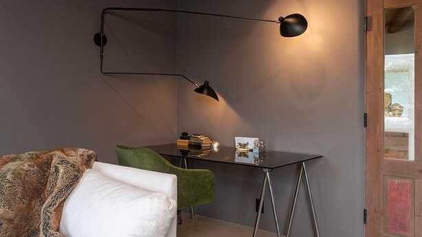 A room with a green chair, a small table with books, and a desk lamp.
