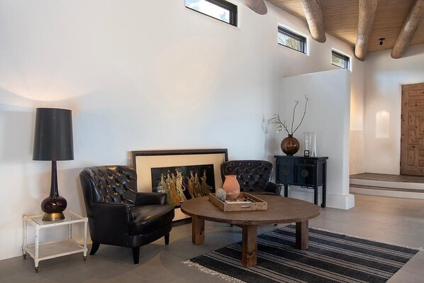A living room with a black leather sofa, a round wooden coffee table, a framed artwork, a side table with a lamp, and a cabinet with decorative items.