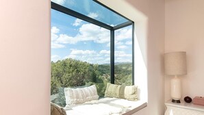 A room with a large window, a white lamp, and a view of greenery.