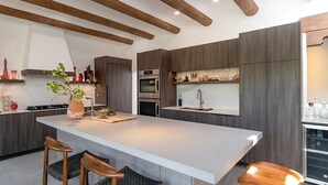 A modern kitchen with a large island, wooden beams, built-in appliances, and bar stools.