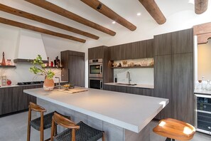 A modern kitchen with a large island, wooden beams, built-in appliances, and bar stools. - Takoda (Santa Fe)