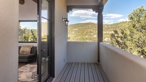 A balcony with a wooden floor, a glass door, a sofa, and a view of a hilly landscape.