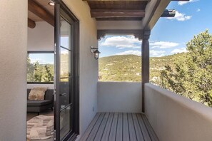 A balcony with a wooden floor, a glass door, a sofa, and a view of a hilly landscape. - Takoda (Santa Fe)